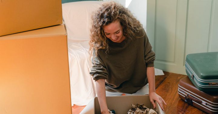 Package Deals - Happy woman unpacking carton box in living room