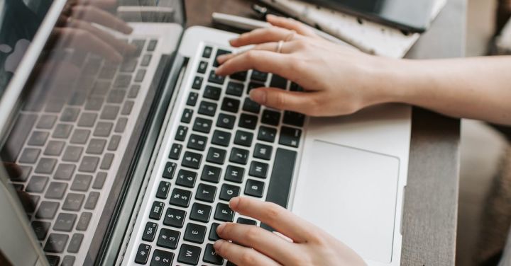 High-Speed Internet - From above of unrecognizable woman sitting at table and typing on keyboard of computer during remote work in modern workspace